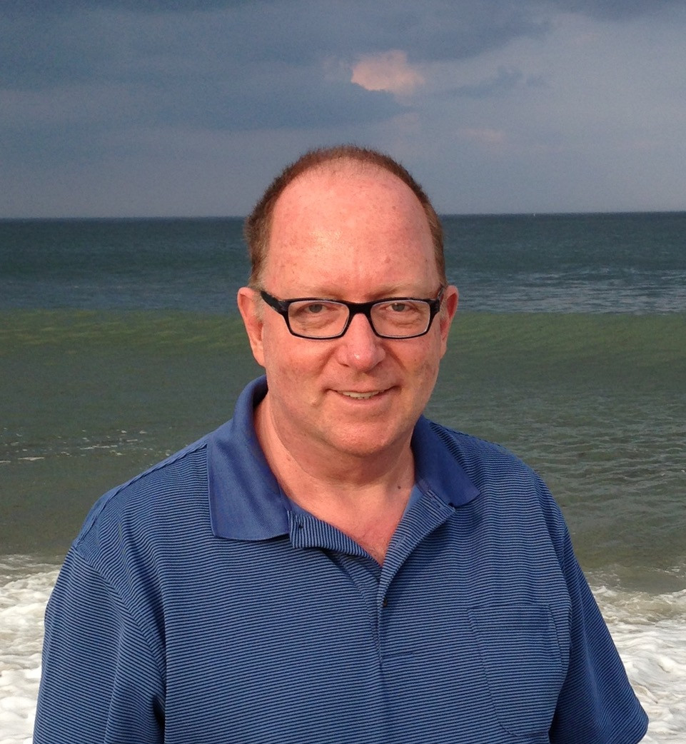 Larry Shepherd in a polo shirt standing on a beach.