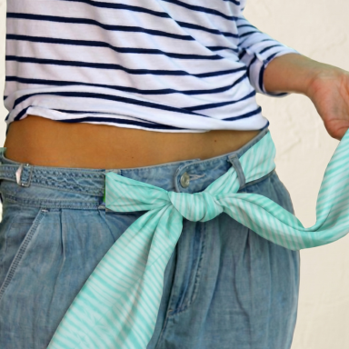 Closeup of model's waist in jeans; green hand-dyed scarf knotted as a belt.