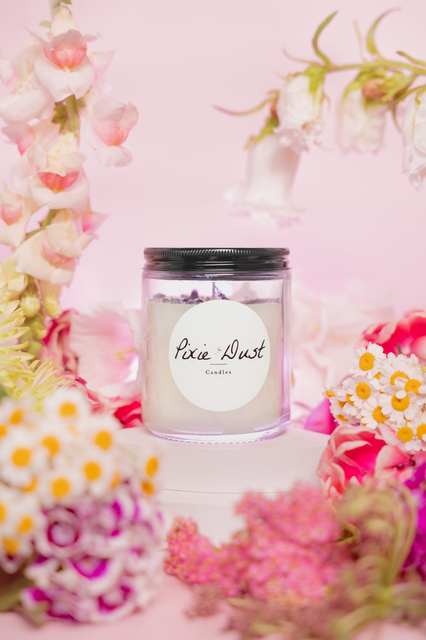 Pixie Dust Candle on a white pedestal surrounded by wildflowers in front of a pink backdrop for business content creation