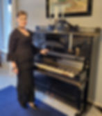 A lady in black evening dress standing in front of and old black piano