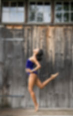 dancer with back leg bent standing against a wood wall
