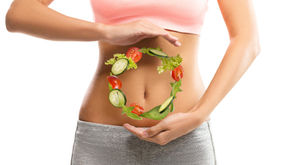 A woman’s hands framing a graphic of a ring of whole plant foods over her stomach, suggesting a healthy gut microbiome