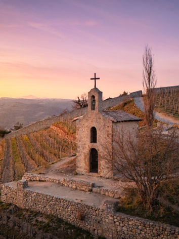 Chapelle en pierre avec croix, vignes et ciel coucher de soleil.