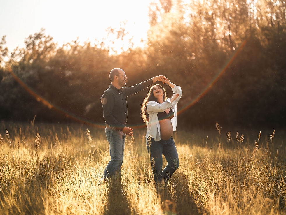 Couple de futurs parents dansant dans un champ doré au coucher du soleil, souriants, baignés de lumière en Drôme
