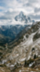 A snow capped mountain piercing the clouds with a dangerous-looking switchback road leading to it ominously.