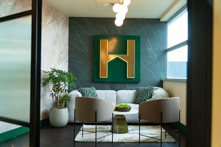 Hope Capital reception lounge with green feature wall, illuminated H branding and upholstered seating.
