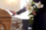 Person laying hand gently on casket of loved one while holding flowers