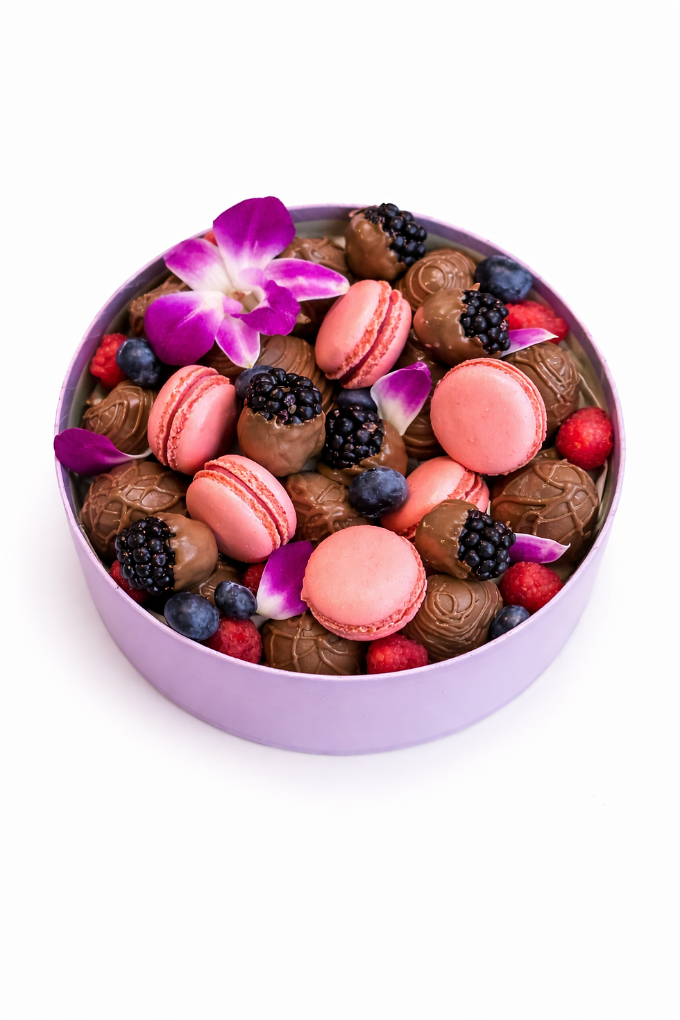A lavender box filled with pink macarons, assorted chocolates, blackberries, blueberries, and red berries, accented by purple