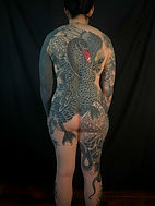 Full back tattoo of a large black swan with wings spread and a vivid red beak. The design features flowers and a snake wrapping around the leg, extending from the shoulders down to the thighs.