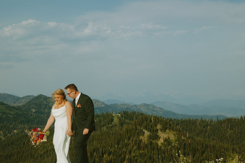 Bride and groom holding hands, walking on a mountain with forested hills in the background for their Glacier National Park elopement.