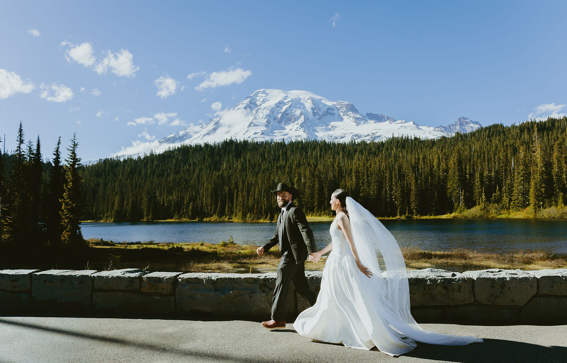 Bride and groom walking beside Reflection Lakes with Mount Rainier behind them during their June elopement
