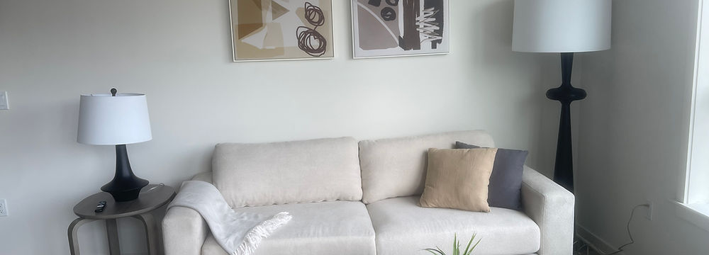 Living room with white sofa, lamps, artwork, and a glass coffee table setting.
