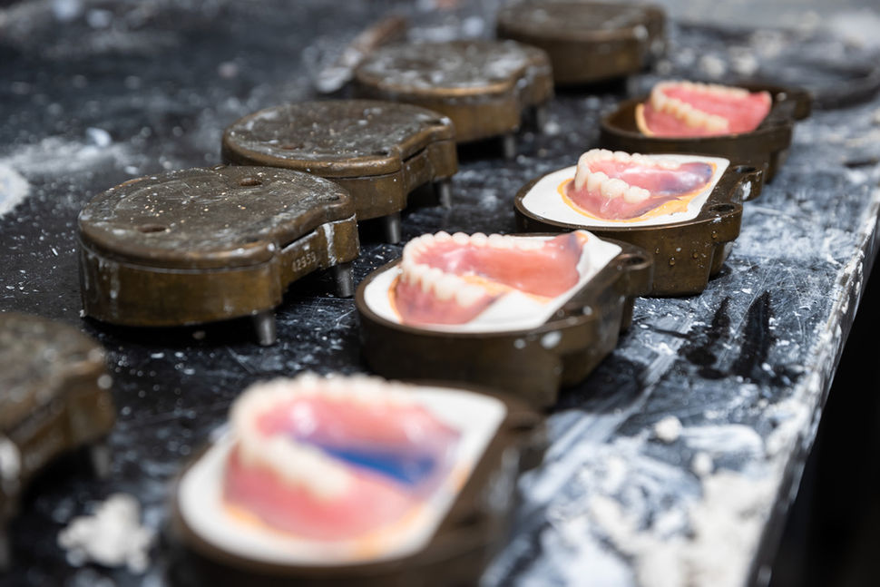 Four finished dentures in ceramic molds lined on a workbench in The Dental Lab.