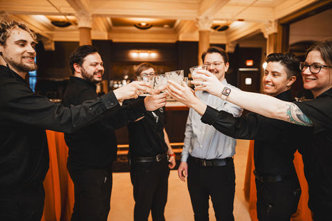 a group of people standing in front the bar, cheersing with cups
