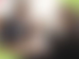 Man in a suit smiles while gesturing in a meeting. Two others listen with laptops. Whiteboard reads "TEAM Training Brainstorms." Bright room.