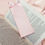 Thumbnail: A pale pink fabric bookmark with a matching ribbon, placed in an open book.