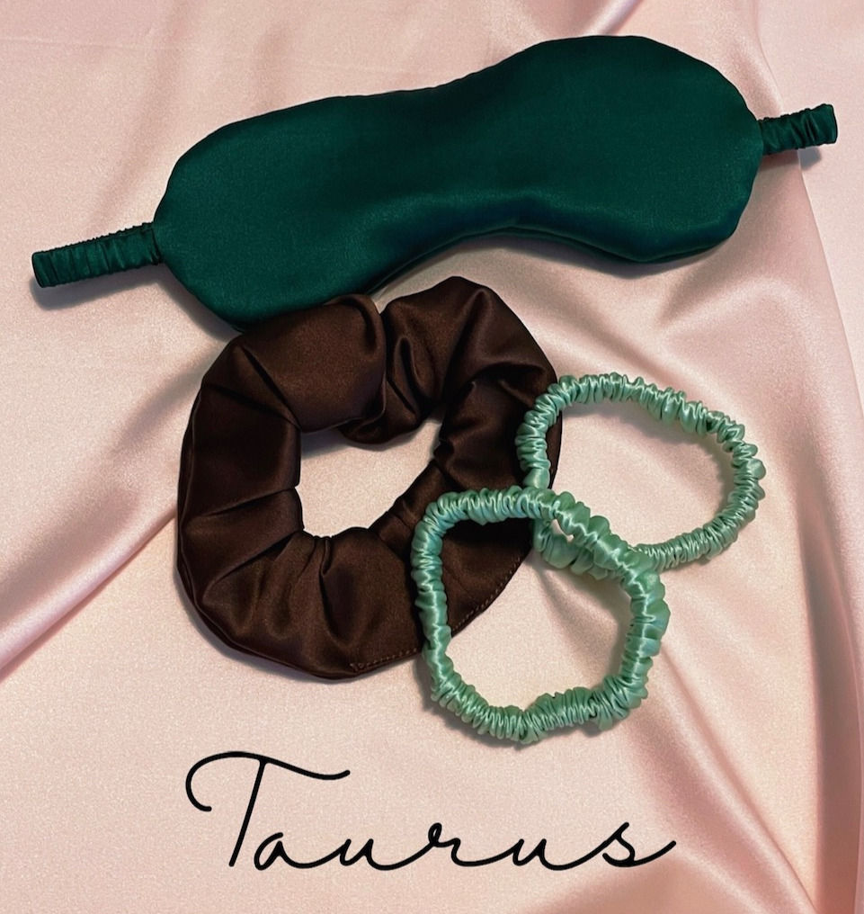 deep green silk eye mask, deep brown scrunchie and two pale mint green silk hair elastics against a pale pink silk background with Taurus text