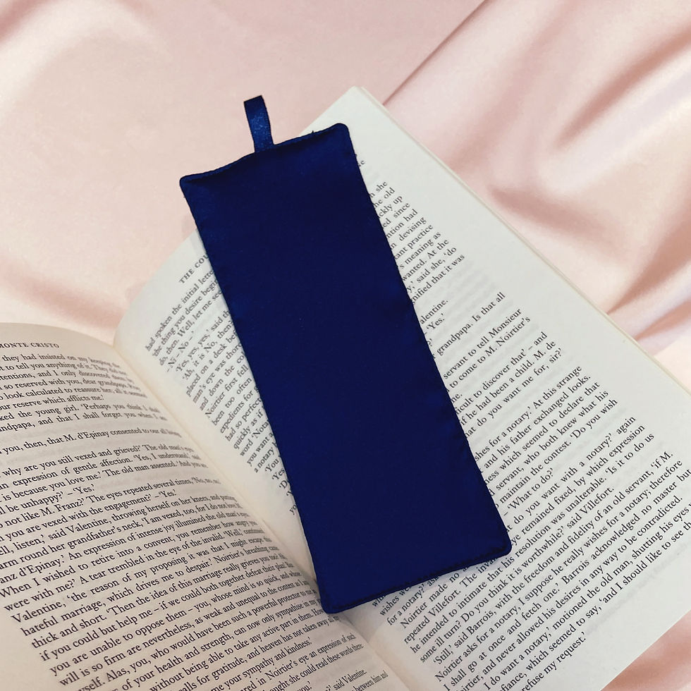 Thumbnail: A dark navy silk bookmark with a ribbon of the same colour, placed in an open book and held by a hand