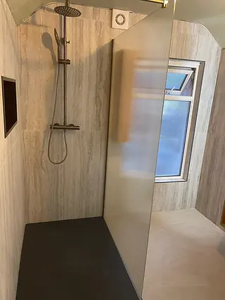 Walk-in shower with a fluted glass screen, black tray, recessed niche and travertine-effect tiles