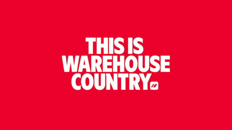 Red poster with bold white text reading THIS IS WAREHOUSE COUNTRY and a small logo on a plain background.