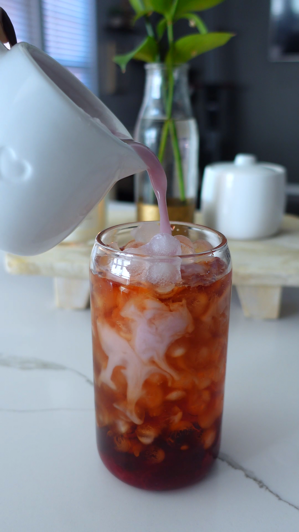 pouring pin cranberry milk into a glass of ice and black tea creating a beautiful swirled effect in the glass