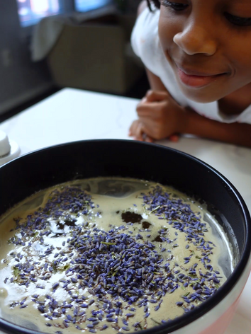Little girl sniffing fragrant pot of dried lavender flowers being made into syrup 