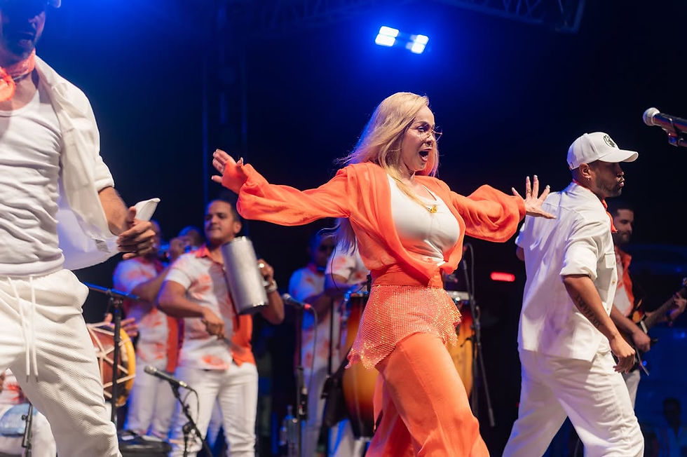 Blonde woman in orange dances onstage with musicians in white and orange under blue stage lights.