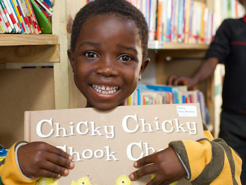 a girl holding a picture book tight to her chest and smiling looking at the camera.