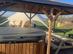 A hot tub under a wooden gazeebo with a bell tent in the background. 