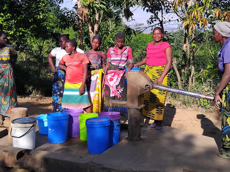 A group of women around the community hand pump with buckets ready to be filled with water.