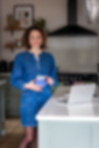 Becks is stood in her kitchen with. a cup of coffee smiling at the camera.