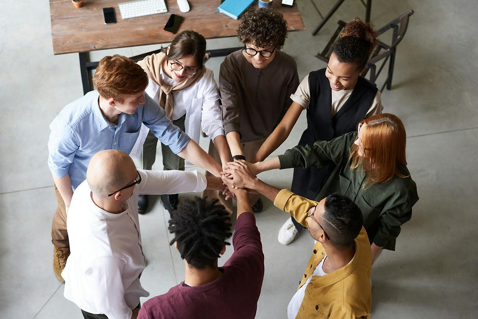Diverse coworkers stack hands in a circle in a bright office, smiling in a team huddle.
