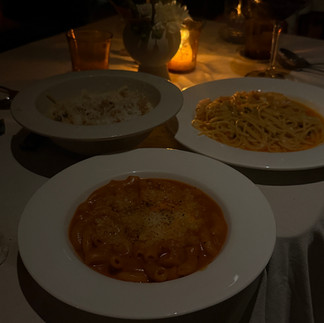 A darkly lit restaurant table with three different pasta dishes