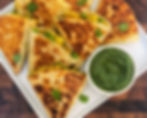Samosa quesadillas on a white plate with a small bowl of coriander chutney.