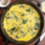 Spinach artichoke frittata topped with black pepper in a cast iron skillet.
