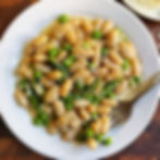 One-pan white beans with asparagus and peas topped with parmesan cheese in a skillet with a spoon beside plates of shredded cheese and freshly grated black pepper.