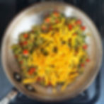 Shreddded cheddar with sauteed vegetables in a pan.