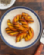 Grilled peaches on a blue-rimmed plate with a fish spatula.