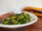 Charred broccoli and sliced flank steak on a plate with a toasted sub roll in the background.