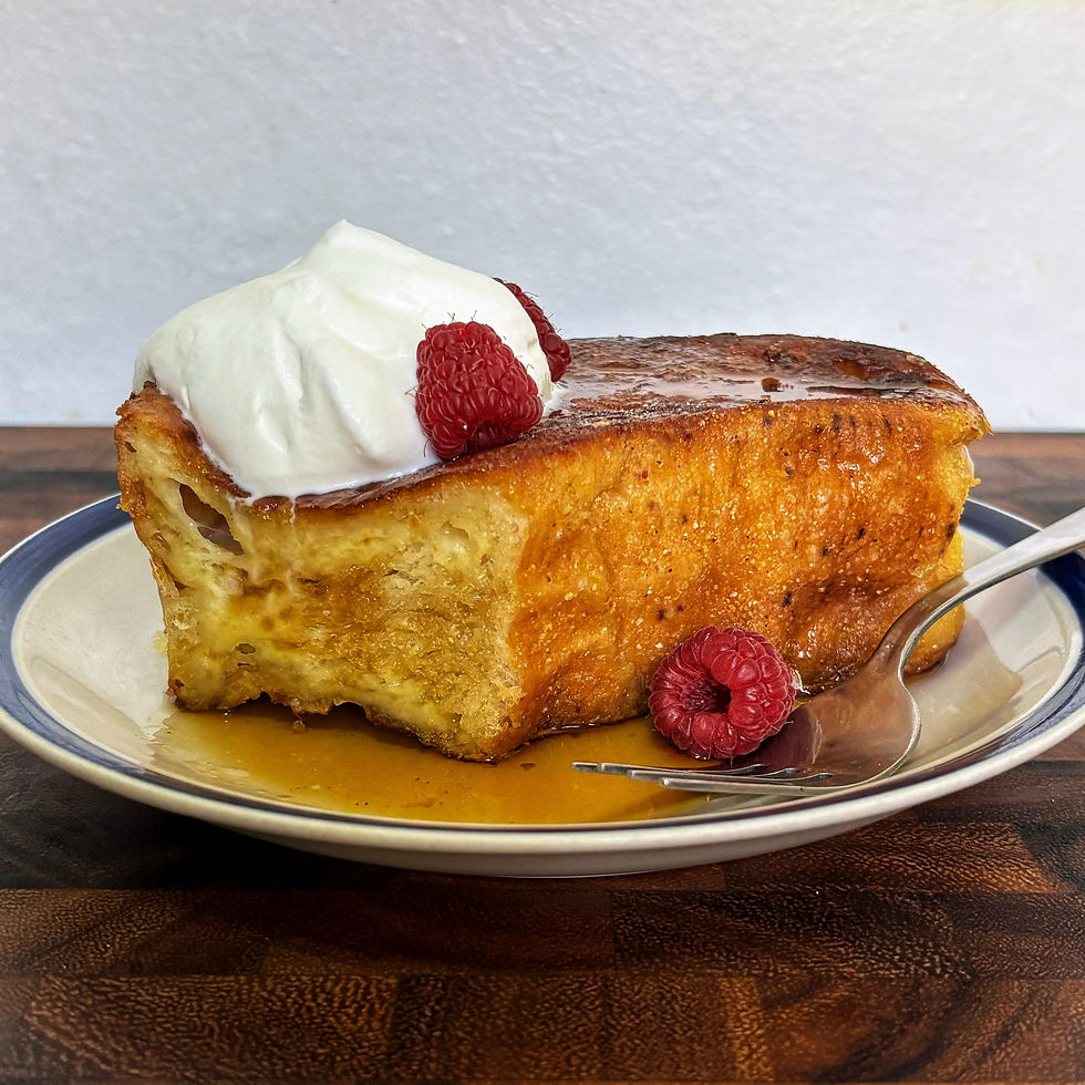 Door-stopping overnight french toast topped with whipped cream, maple syrup, and raspberries on a plate with a fork.
