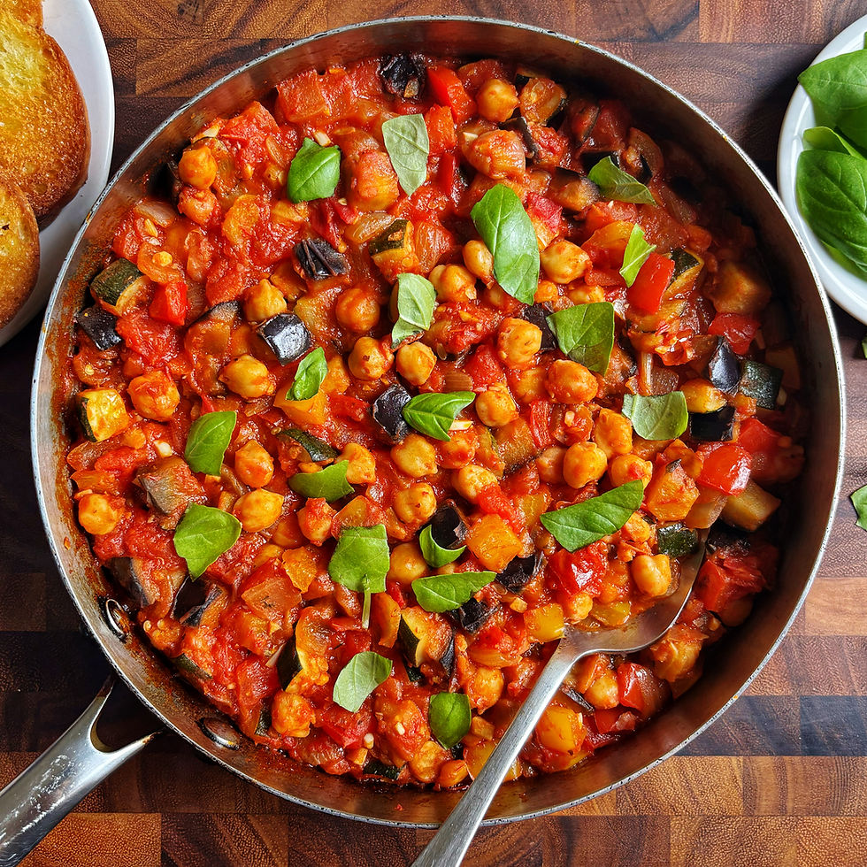 Ratatouille with chickpeas topped with fresh basil in a pan.