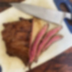 Flank steak sliced on a cutting board with a knife.