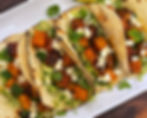 Roasted squash adobo tacos with brussels sprout slaw, queso fresco, and cilantro on a white platter with lime wedges.