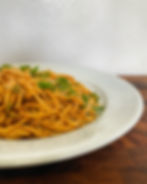 Spicy sesame noodles topped with scallions and sesame seeds on a white plate.