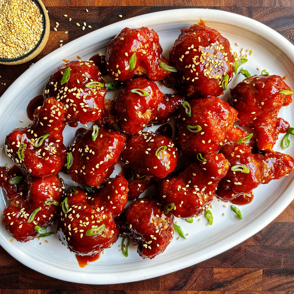 Oven-fried cauliflower wings tossed in Koran BBQ sauce on a platter topped with sesame seeds and scallions.
