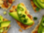 Crispy rice cakes topped with sriracha, avocado, cucumber, and scallions on white parchment paper.