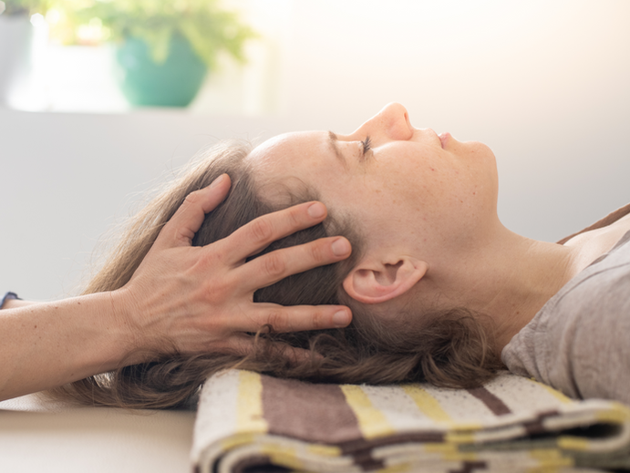 a woman is resting face up on a table while the practitioner gently holds her head