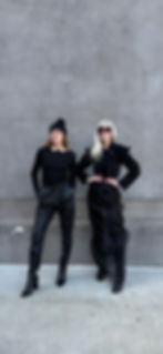 two women in stylish all black outfits by grey wall