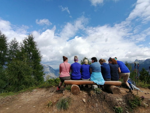 Eine Frauengruppe sitzt bei einer Wanderung entspannt auf einer Bank und genießt die schöne Aussicht und das Panorama in den Berchtesgadener Alpen
