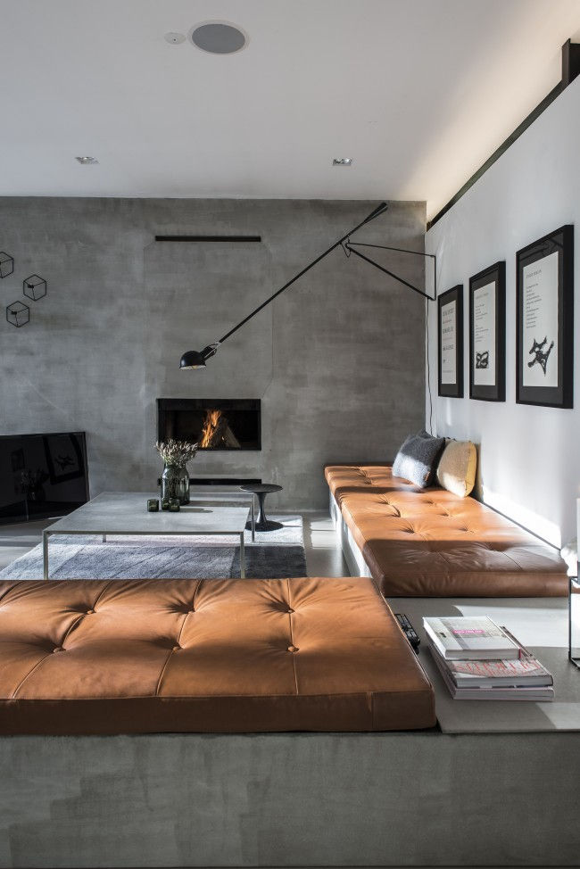 Living modern cu șemineu aprins, banchete maro din piele, lampă neagră de perete, tablouri pe perete și masă cu flori și reviste.